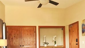 A bedroom with a bed, a ceiling fan, wooden doors, and a small shelf with flowers. - Wesbert Winery & Guest Suites (Penticton)