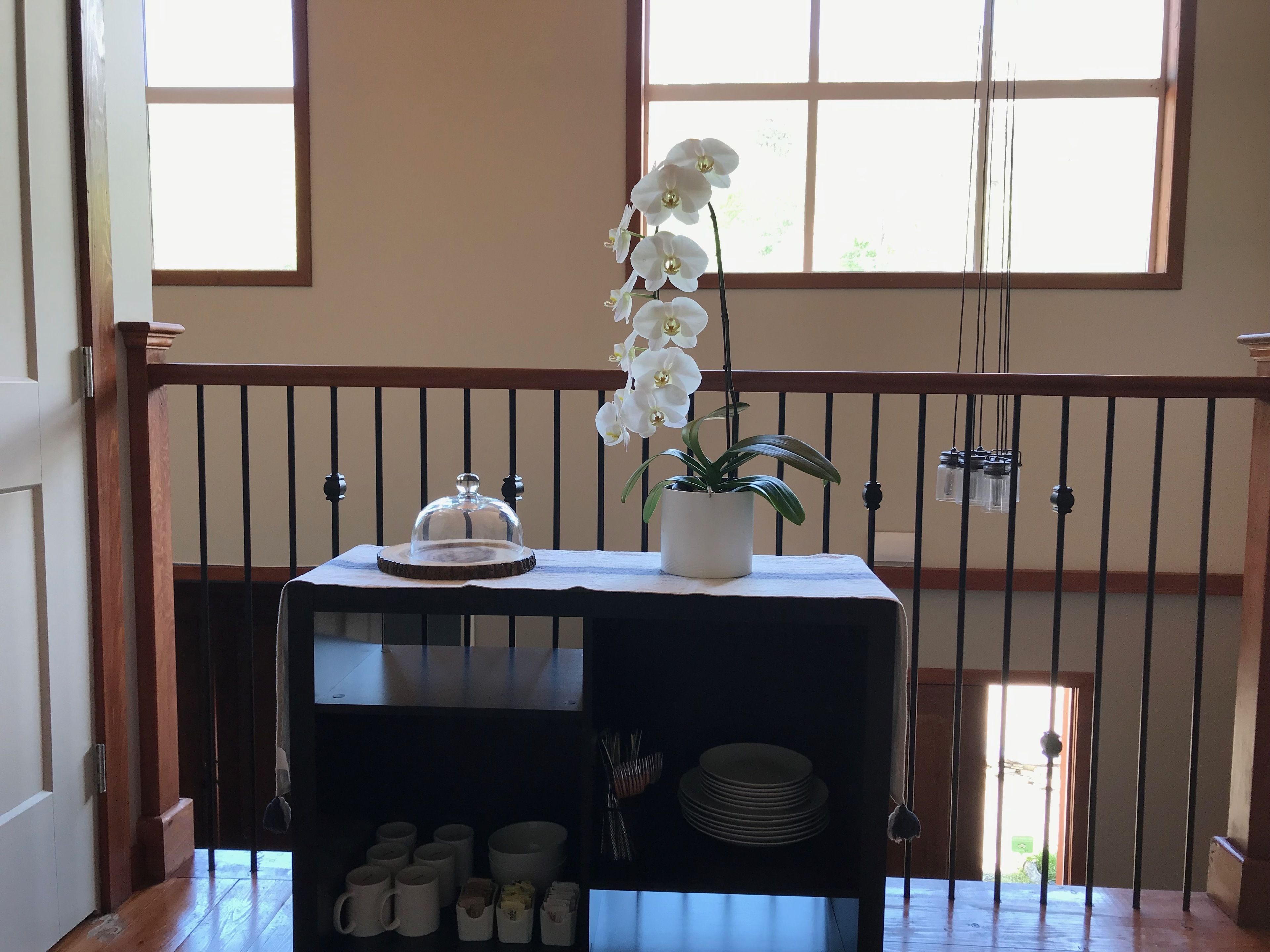Una mesa con una lámpara de cristal en el centro, una orquídea en maceta y una bandeja de platos blancos.
