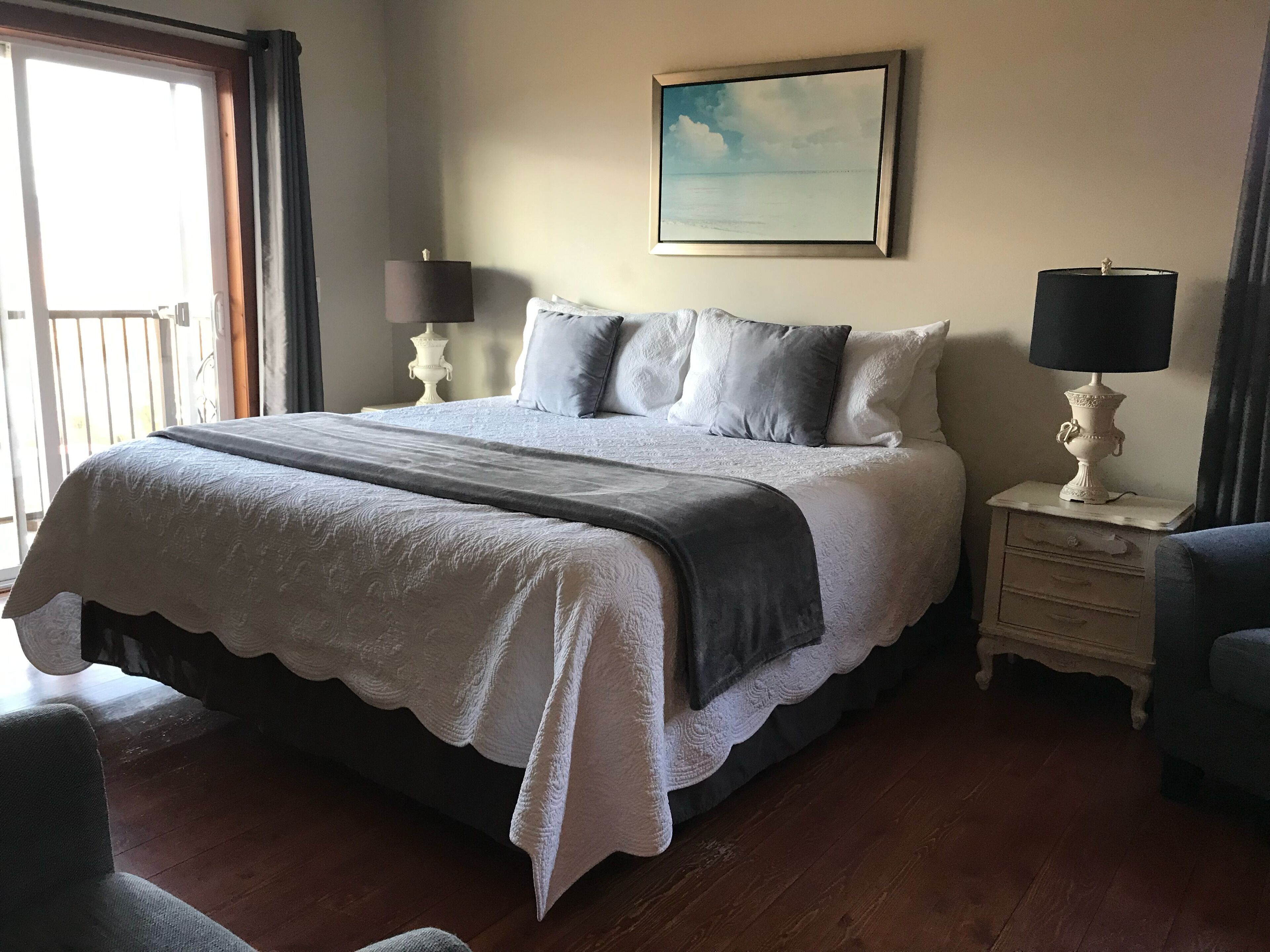 A neatly made bed with a white and gray duvet, a bedside table with a lamp, and a painting on the wall.