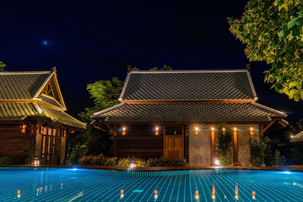 A traditional building with a tiled roof, a swimming pool in front, and a tree to the right.