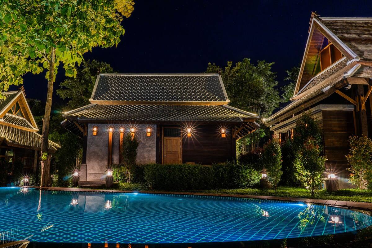 A poolside view of a building with a tiled roof and multiple windows, surrounded by greenery.
