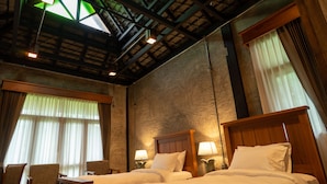 Une chambre d’hôtel avec deux lits, une tête de lit en bois, une chaise et une grande fenêtre avec des rideaux.