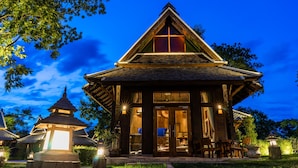 Un bâtiment en bois doté d’un toit triangulaire et d’une grande fenêtre, entouré de verdure et éclairé par un éclairage d’ambiance.