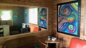 Interior de una cabaña de madera con pared espejada, zona de comedor y un cuadro abstracto grande.