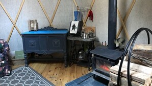 Una habitación con tienda de campaña, un aparador azul, una mesita con un hervidor y un estufa de leña.