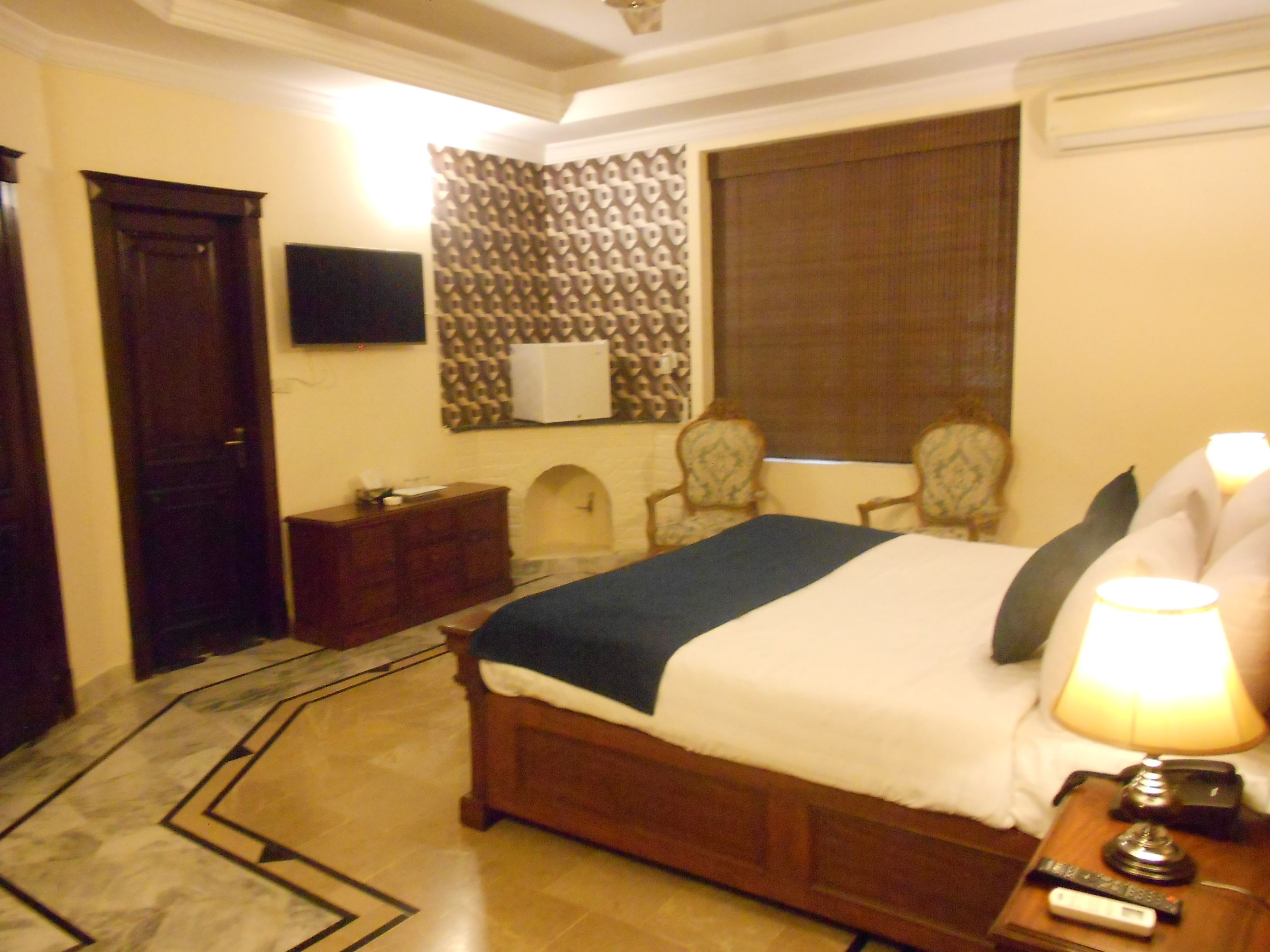 Une chambre d’hôtel avec un lit, une table de chevet, un téléviseur, un mur décoré d’un motif et une fenêtre avec des rideaux.