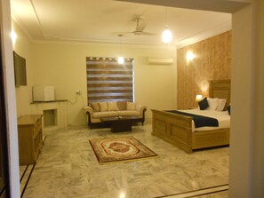A bedroom with a bed, a sofa, a coffee table, a TV, and a wooden wall. - Hospitality Koncepts (Islamabad)