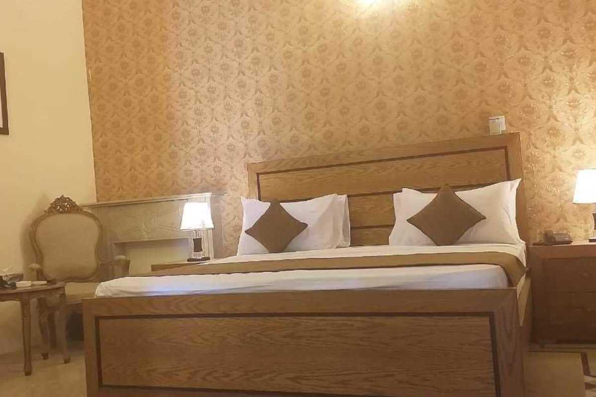 A neatly arranged hotel room with a wooden bed, two bedside tables with lamps, a chair, and a framed picture on the wall.