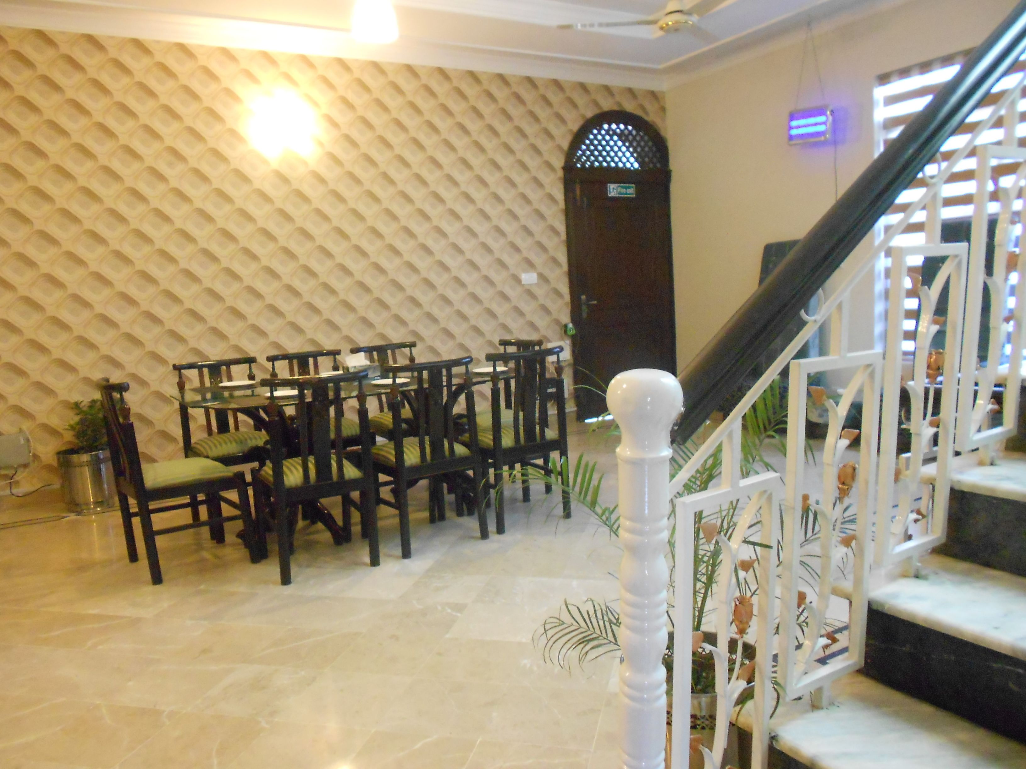 A lobby with a patterned wall, a staircase with white railings, and several wooden chairs with cushions.