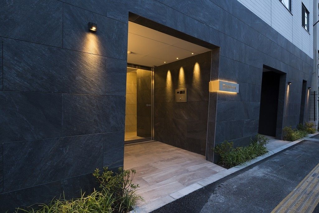 A modern building entrance with a dark facade, a glass door, and a small sign above the door.