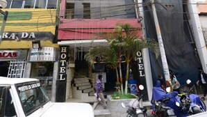 Un edificio de varios pisos con un letrero de hotel, una entrada visible y vehículos estacionados.