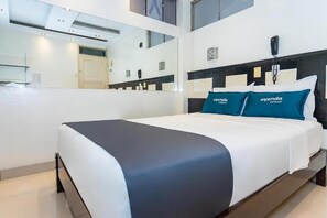 Una habitación de hotel con cama, teléfono junto a la cama y un espejo.