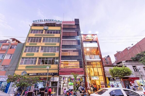 Un hotel de varios pisos con un cartel llamativo, múltiples balcones y una animada calle.