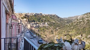 A street with buildings on a hillside, a clear sky, and a distant view of a town. - Ad Maiora - Desing Rooms (Ragusa)