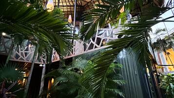 Ein Gebäude mit einem Reetdach und einer Holzterrasse, umgeben von üppiger tropischer Vegetation.