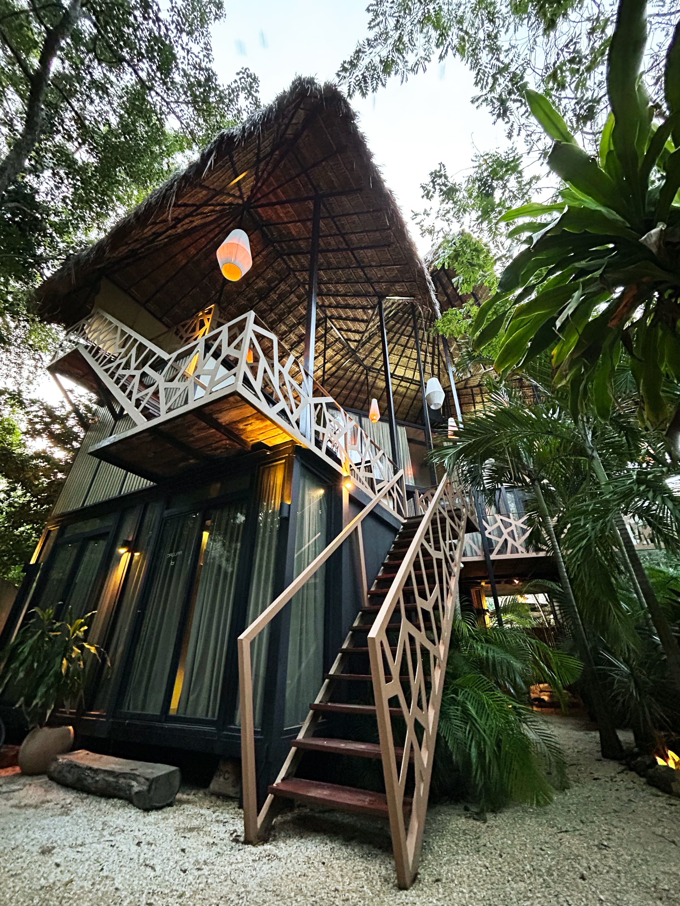 Une construction à toit de chaume, dotée d’un escalier en bois menant à un balcon.