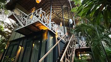 A thatched-roof structure with a wooden staircase leading to a balcony.