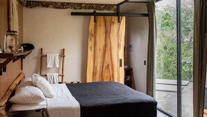 A modern bedroom with a large bed, wooden headboard, and a view of greenery through the window. - Bufo Alvarius (Tulum)