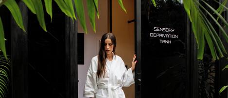 Una persona con bata blanca de pie en la entrada de un edificio con un letrero que dice 'SENSORY DEPRIVATION TANK'.