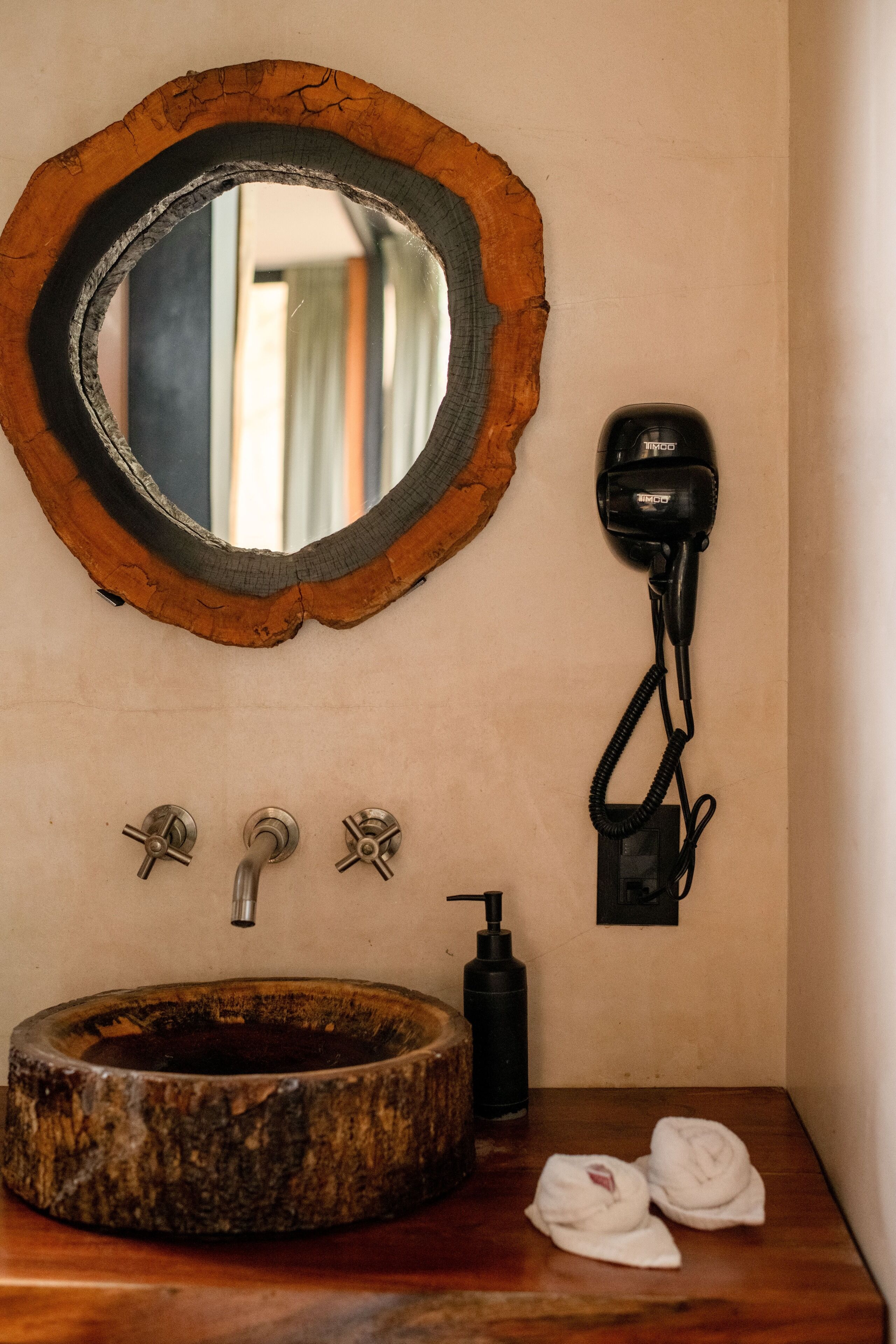 Ein Badezimmer mit einem rustikalen Holzbachttisch, einem runden Spiegel und einem an der Wand montierten Föhn.