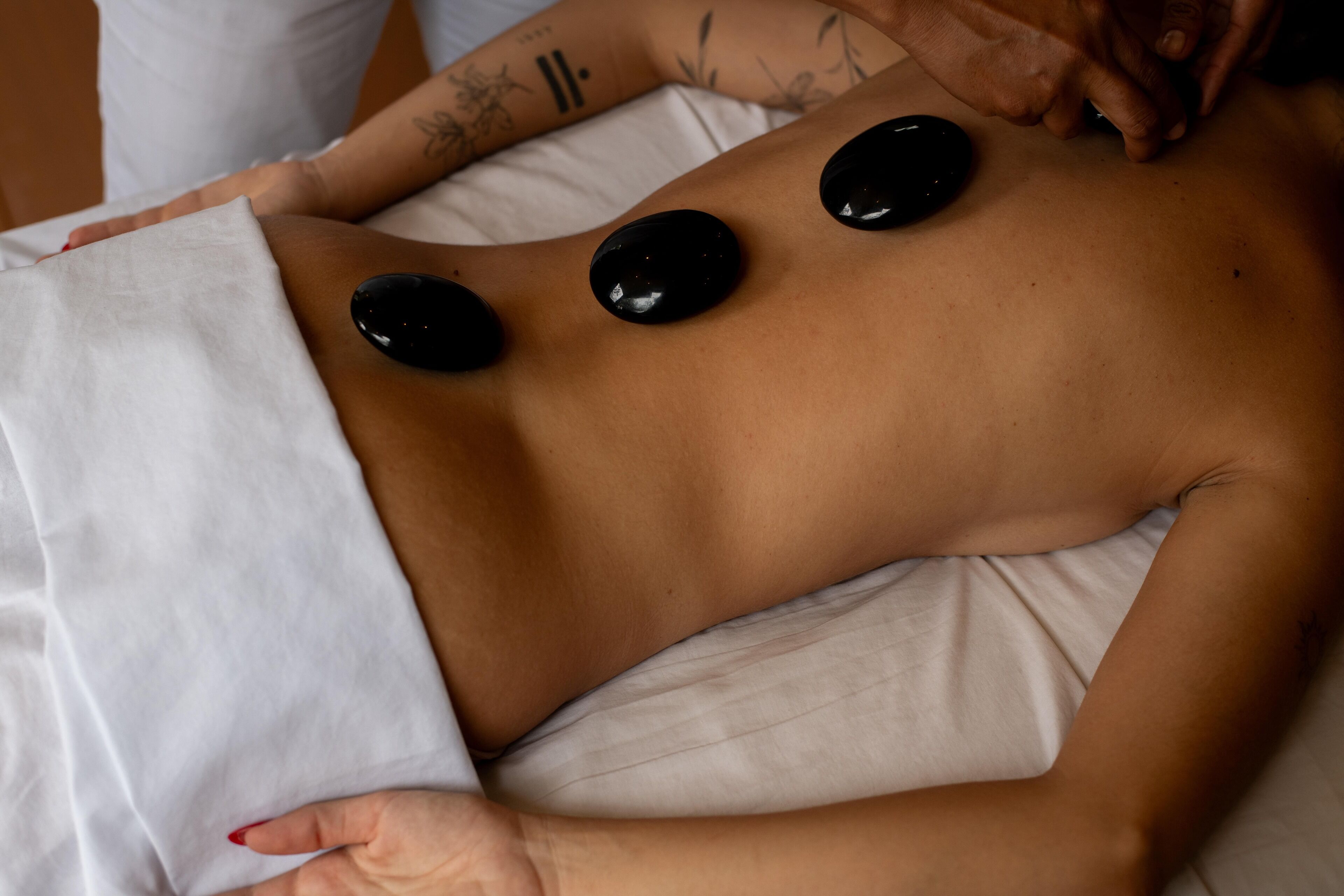 A person receiving a back treatment with three black stones placed on their back.