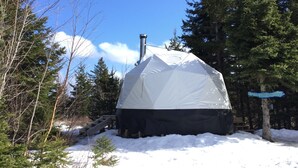 Un igloo enneigé, doté d’une cheminée, entouré d’arbres et auquel on accède par un escalier en bois.