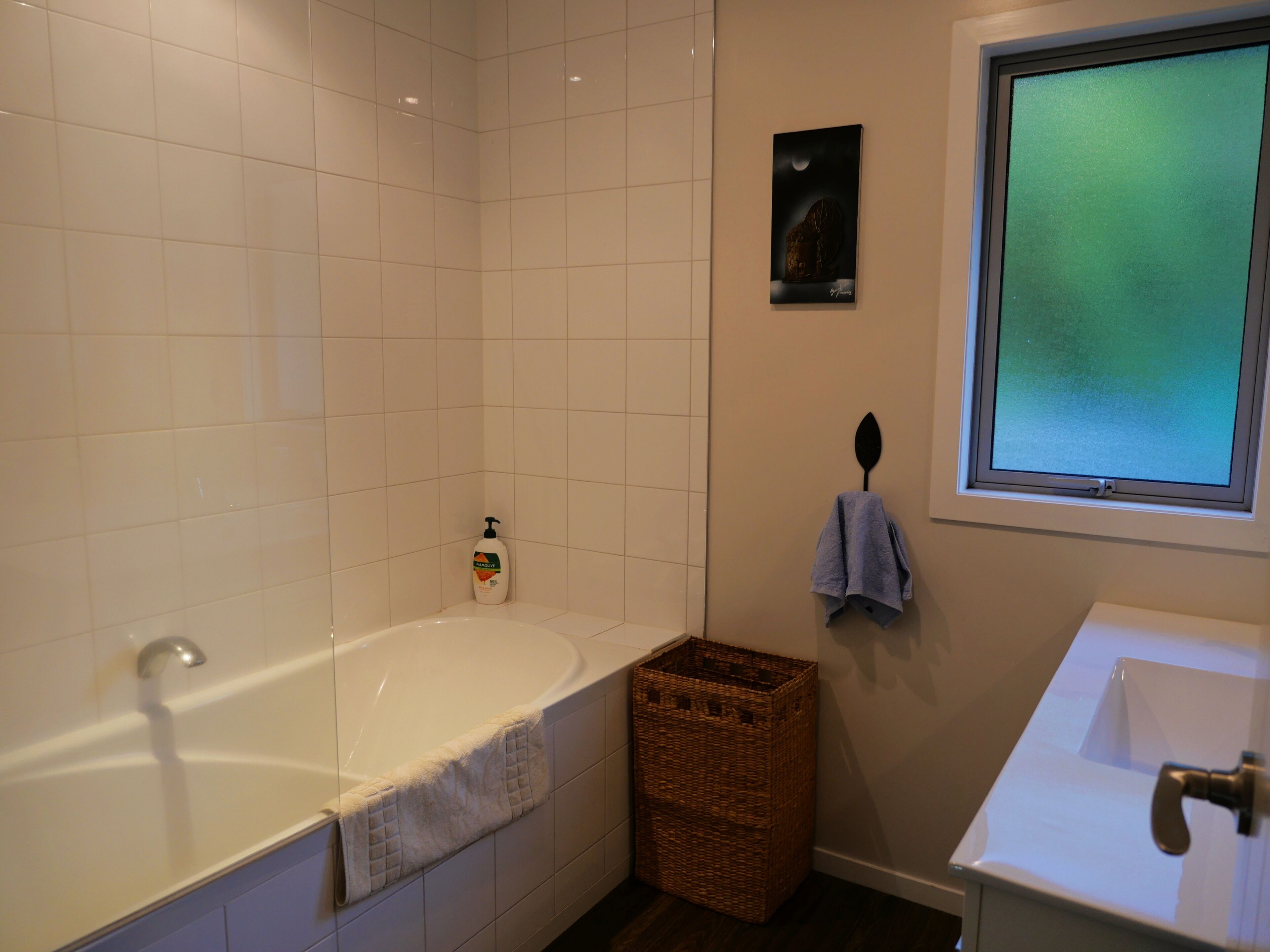 Une salle de bain avec une baignoire, un lavabo, une fenêtre et un porte-serviettes fixé au mur.