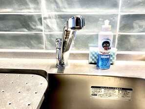 A stainless steel sink with a chrome faucet, a bottle of Joy W detergent, and a sponge.