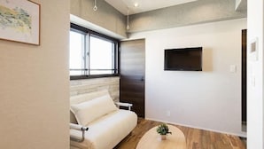 A modern living room with a sofa, a round wooden coffee table, and a TV mounted on the wall. - A9 Haneda Maison Philippe Omori 901 (Tokyo)