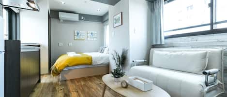 A compact hotel room with a bed, a sofa, a small table, and a kitchenette.