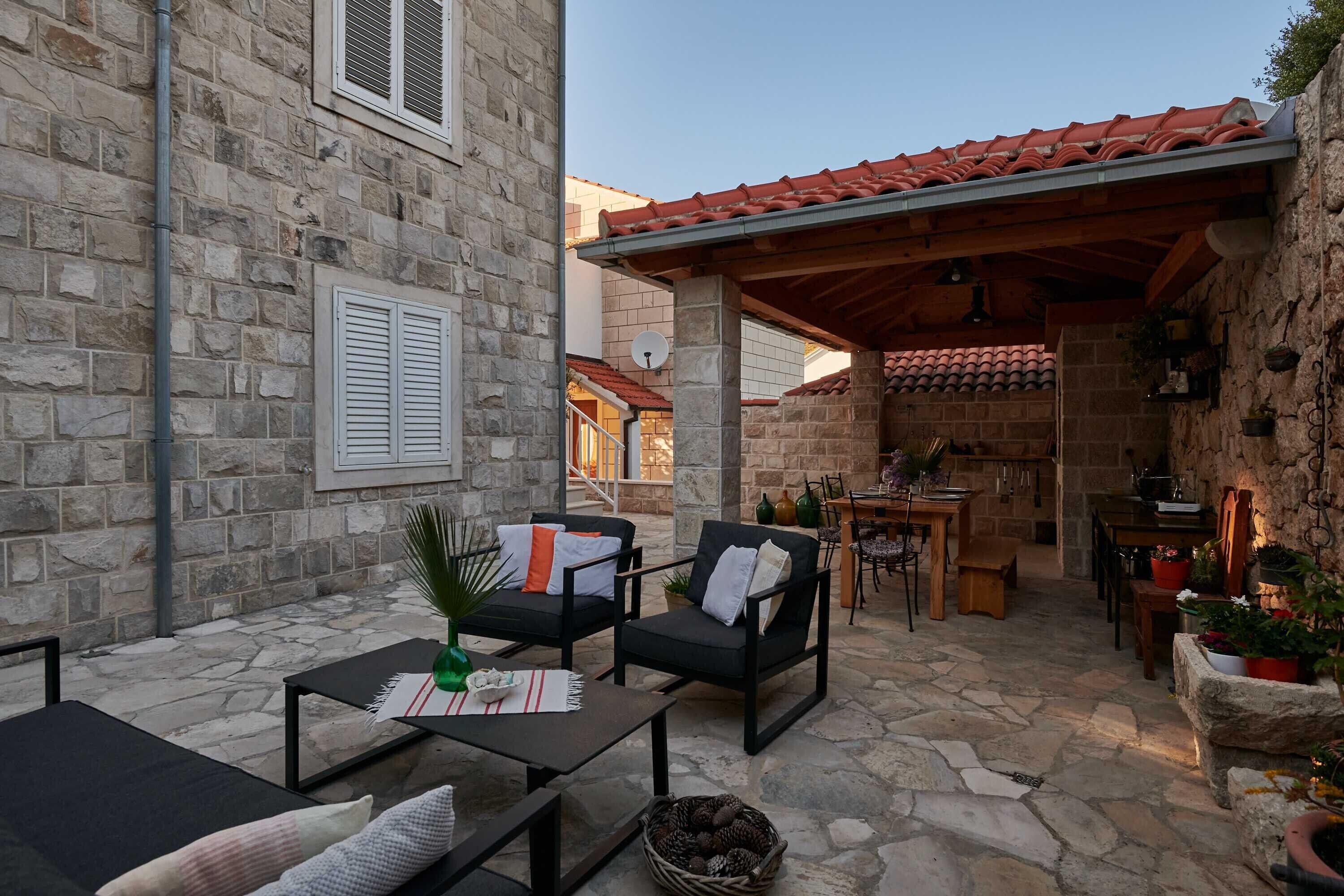 Un bâtiment en pierre doté d’un patio aménagé avec du mobilier d’extérieur, une table à manger et un coin cuisine avec des meubles en bois et des plantes en pot.