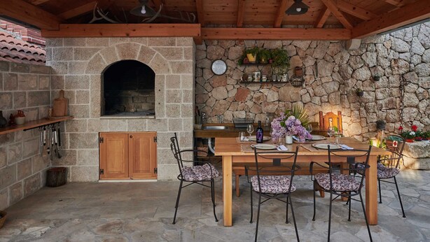 An outdoor dining area with a stone wall, wooden ceiling, and a stone fireplace. - Apartments Micika - Comfort Studio Apartment with Balcony and Sea View (A2) (Zvekovica)