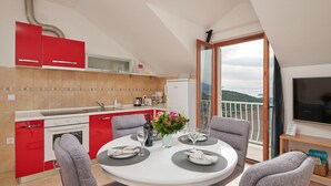 A modern kitchen with red cabinets, a dining area with a round table, and a balcony with a TV. - Apartments Micika - Comfort Studio Apartment with Balcony and Sea View (A2) (Zvekovica)