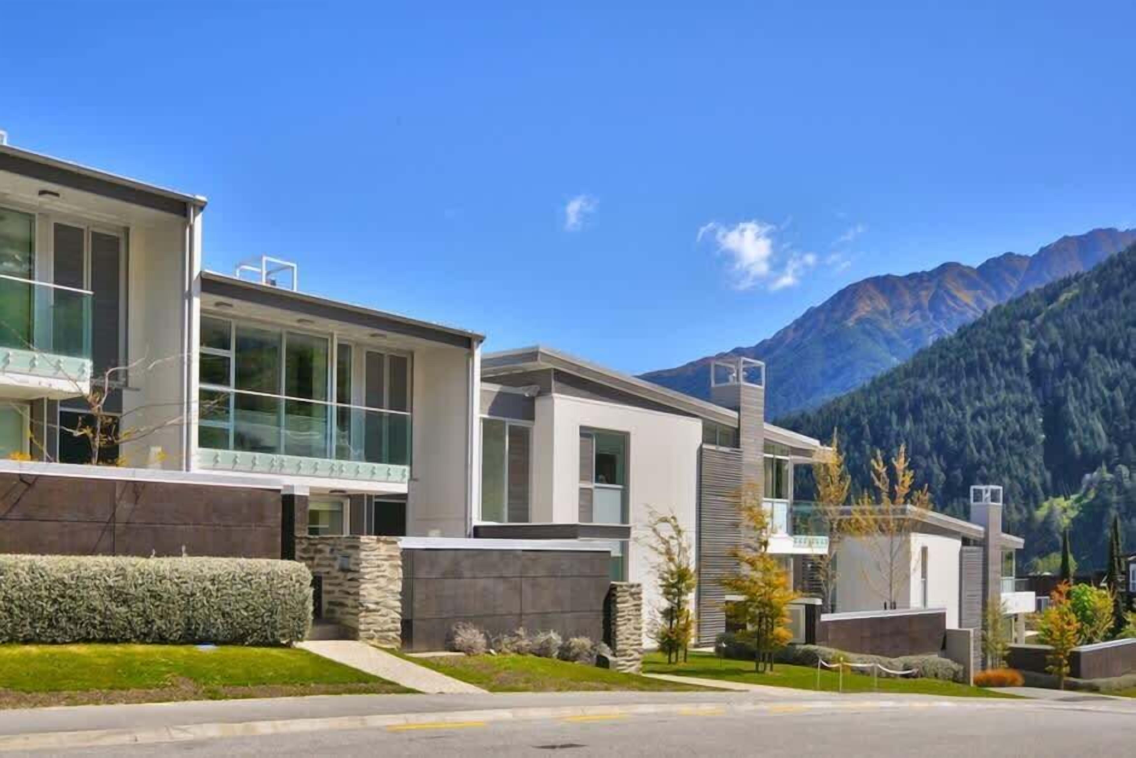 Un bâtiment moderne doté de grandes fenêtres et d’une façade en pierre, qui se détache sur un paysage montagneux.