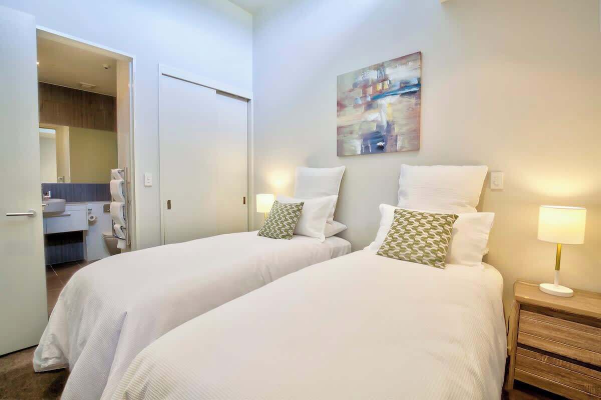 A hotel room with two beds, a bathroom visible through an open door, and a painting on the wall.