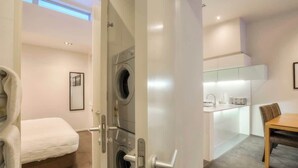 Ein modernes Hotelzimmer mit Waschmaschine, einem Bett, einem Essbereich und einer Küchenzeile.