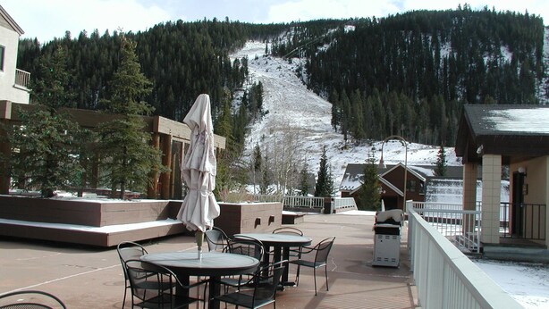 Een terras met buitenmeubilair, een overdekte parasol en uitzicht op een besneeuwde berg.