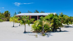 A beach house with a white roof and red-framed windows, surrounded by palm trees and sand. - 🌴 Sundial Villas ~ Conch Coastal Calm (Bambarra Beach)