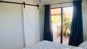 A bedroom with a bed, a sliding door, and a view of an outdoor deck. - 🌴 Sundial Villas ~ Conch Coastal Calm (Bambarra Beach)