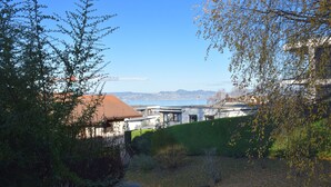 A view of a modern building with a red roof, surrounded by greenery and overlooking a body of water with distant mountains. - Cozy apartment with terrace, Wi-Fi, and parking in Évian-les-Bains (Évian-les-Bains)