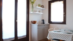 A kitchen with a dining table set for four, a coffee maker, and a vase with flowers on the counter. - Cozy apartment with terrace, Wi-Fi, and parking in Évian-les-Bains (Évian-les-Bains)