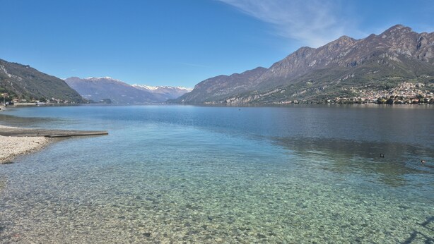 A clear lake with rocky shore, mountains in the background, and a small dock. - Lakeside cottage with private garden and pier. Pet-friendly.  (Oliveto Lario)
