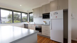 A modern kitchen with a large island, stainless steel appliances, and a view of the outdoors through large windows. - Jinalong - Breathtaking Views (Angourie)