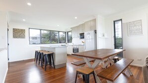A modern kitchen with a central island, bar stools, and a dining table with benches. - Jinalong - Breathtaking Views (Angourie)