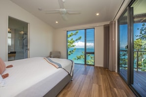 Une chambre avec un lit, un ventilateur de plafond, une porte-fenêtre coulissante donnant sur un balcon et une vue sur la mer.