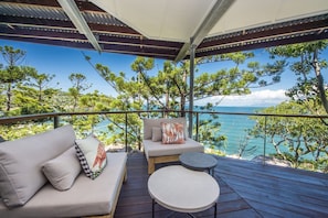 Ein Balkon mit einer Couch und einem kleinen Tisch, mit Blick auf eine Küstenlandschaft mit Bäumen und dem Meer.