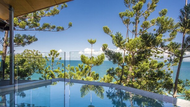 Vista despejada de una piscina con borde de cristal, rodeada de árboles y con vistas a una masa de agua.
