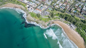 An aerial view of a coastal area with a beach, residential buildings, and a road network.