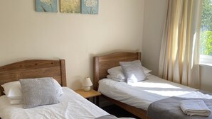 Habitación de hotel con dos camas de madera, ropa de cama blanca, una lámpara en una mesita de noche y una obra de arte en la pared.