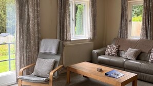 Una sala de estar con una mesa de centro de madera, un sillón gris, un sofá con cojines estampados y un radiador.